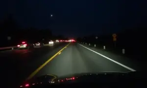 Carro utilizando farol alto em rodovia à noite, tráfego no sentido oposto.