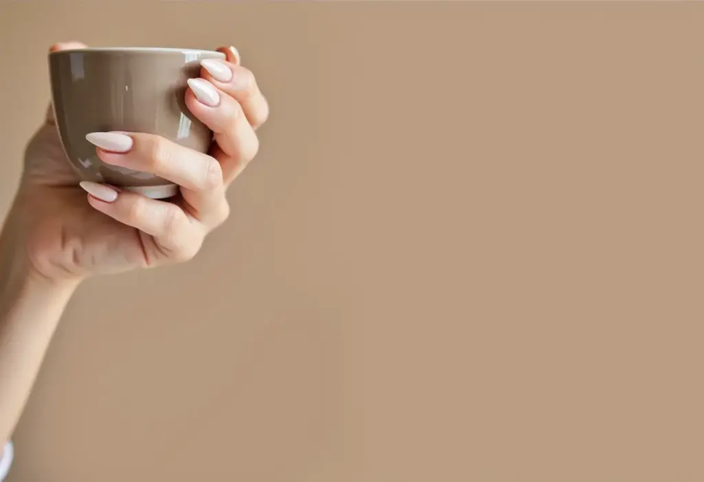Unhas Amendoadas: O segredo para mãos elegantes e modernas Unhas amendoadas cor nude segurando xícara de chá