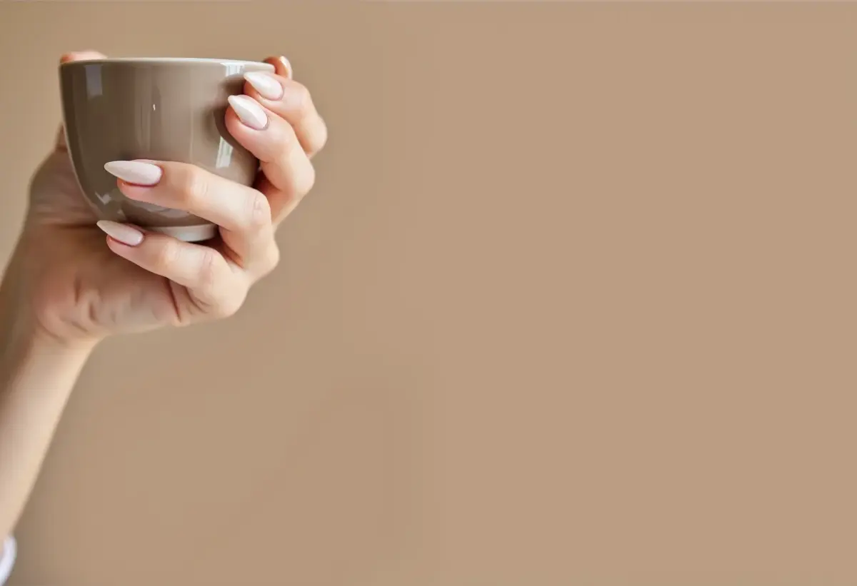 Unhas amendoadas cor nude segurando xícara de chá